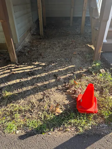 Cleared ground beneath a raised deck with a safety cone nearby